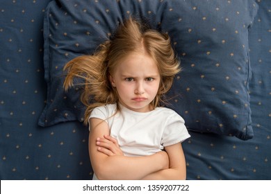 Angry Child Girl Lying On The Bed With Crossed Hands And Refuses To Sleep