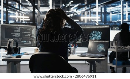 Angry computing hub software developer frustrated by slow data analytics AI generator, while annoyed server facility staff member punching desk, irked by buggy AI program showing system metrics.