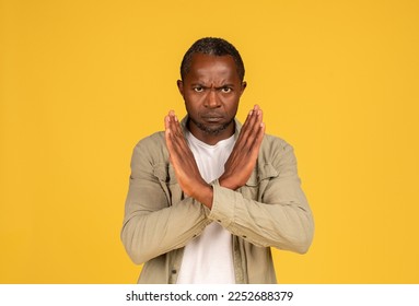 Angry confident sad middle aged african american man in casual crossed arms, doing stop sign isolated on yellow background, studio. Fight against discrimination, violence gesture and covid-19 virus - Shutterstock ID 2252688379