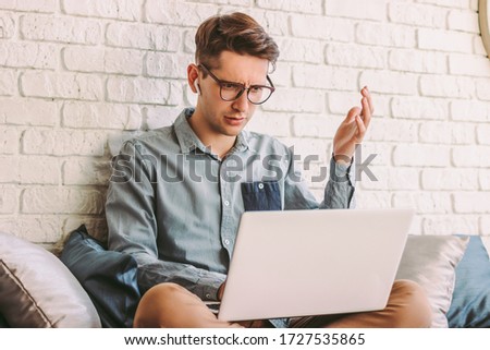 Angry confused businessman freelancer feel irritated while use laptop for work at home. Puzzled impatient hipster man in glasses impressed by bad news from computer. Emotional surprised man on couch