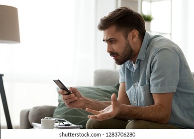 Angry Confused Man Holding Discharged Phone Annoyed By Spam Message, Missed Call Or Bad Mobile Signal Looking At Smartphone, Mad Male Customer Frustrated By Cellphone Problem Receiving Bad News