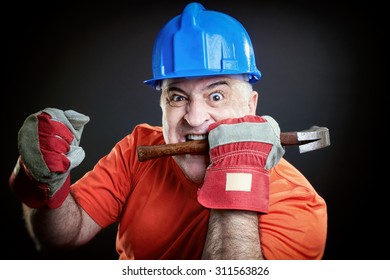 Angry construction worker with helmet and hummer. Mad worker biting hammer showing fist.