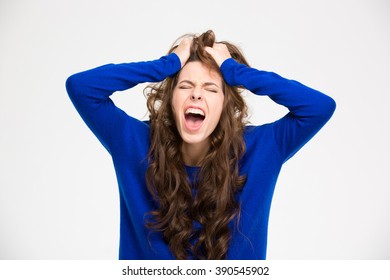 Angry crazy young woman with long curly hair screaming over white background 