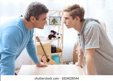 Angry Dad And Son Look At Each Other While Standing At Home. Serious Dad And Son Look At Each Other With Serious And Angry Faces.