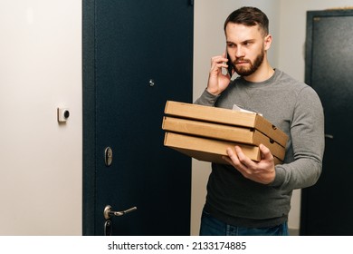 Angry Delivery Man Standing By Door Of Customer Apartment With Boxes Of Hot Pizza And Calling Customer On Phone. Courier Having Problem With Delivery Of Online Order To Client.