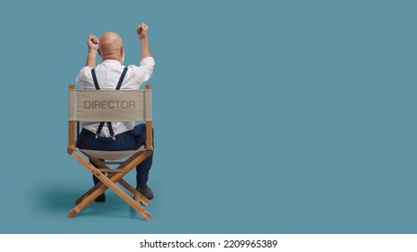 Angry Disappointed Film Director Sitting On The Director's Chair And Shouting With Raised Fists