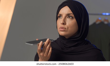 Angry displeased Islamic Muslim Arabian woman model lady speaking talk loudspeaker negotiate mobile phone smartphone call. Annoyed girl in hijab female record audio voice message voicemail in studio - Powered by Shutterstock