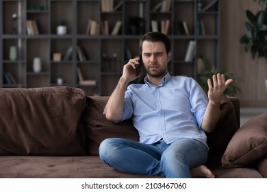 Angry Dissatisfied Man Talking On Phone, Arguing Or Solving Problem, Sitting On Couch At Home, Irritated Unhappy Client Having Unpleasant Conversation With Customer Support Service, Complaining