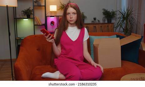 Angry dissatisfied shopper teen redhead children girl unpacking parcel feeling upset confused with the wrong delivery from an online store, bad quality purchase at home. Kid indoor in room on couch