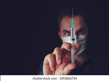 Angry doctor woman in a medical mask holds a syringe on an isolated in a dark background. evil doctor. Unskilled medicine. bad doctor. crazy,mad, insane, daft,madman, lunatic,