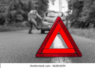 Angry Driver Kicking The Tires On Broken Car And Red Warning Trangle - Black And White Concept