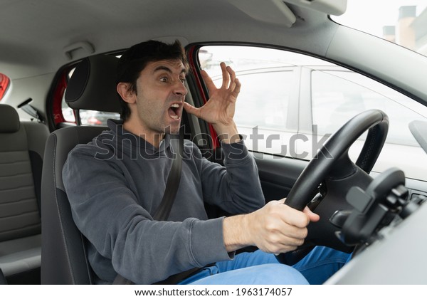 Angry driver stuck in traffic jam gesticulates\
with hand and screaming. Crazy man yelling from car desperately.\
Stress, traffic rush hour\
concepts