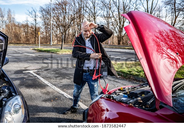 Angry driver trying to start broken car with\
jumper cables