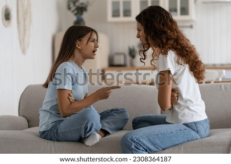 Angry emotional teen girl adolescent daughter fighting with mother parent at home while sitting in front of each other on sofa, selective focus. Problems between teenagers and parents