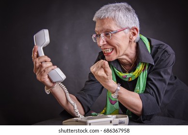 Angry, Enraged Senior Woman Yelling At A Landline Office Phone, 