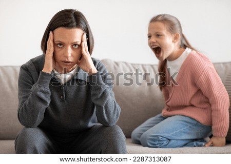 Angry excited aggressive teenager european girl yelling at sad tired millennial woman in living room interior. Relationship problems between mother and daughter, quarrel, hysteria