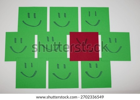 An angry face sticky note surrounded by happy smiley notes. Concept of mental health, isolation, mood contrast, emotional differences, depression awareness and social pressure to stay positive.