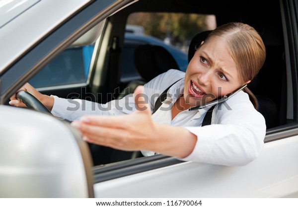 angry female driving the car, holding the mobile\
phone and screaming at\
someone