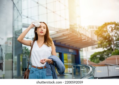 Angry female having sunstroke skin damage from sun UV city air pollution outside on street, Overheating Asian beautiful business woman drying sweat her face with cloth in warm summer day hot weather