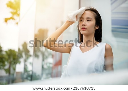 Angry female having sunstroke skin damage from sun UV city air pollution outside on street, Overheating Asian beautiful business woman drying sweat her face with cloth in warm summer day hot weather