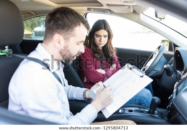 Angry female learner looking at\
driving coach rejecting license application in\
car