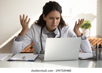 Angry Female Nurse Work On Laptop In Clinic Frustrated By Slow Internet Connection On Gadget. Unhappy Mad Woman Doctor Use Computer In Hospital Confused With Operational Problem Or Spam On Device.