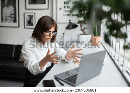 Angry frowning young businesswoman working online on laptop pc computer, getting video call or reading emails and gesturing, sitting at coworking space, copy space