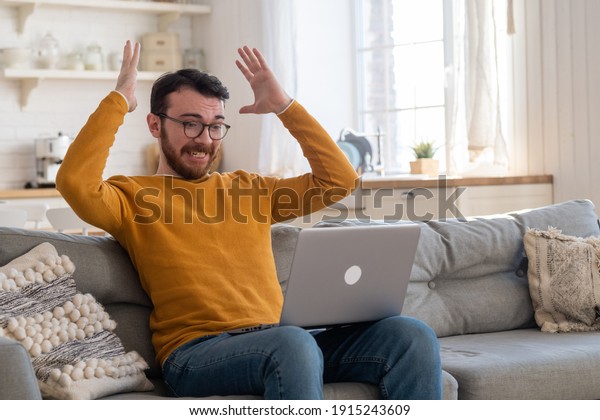 Angry frustrated annoyed young adult man consumer\
feel rage looking at computer notebook screen furious about laptop\
pc problem, bad software failure, system virus or malfunction sit\
at home table