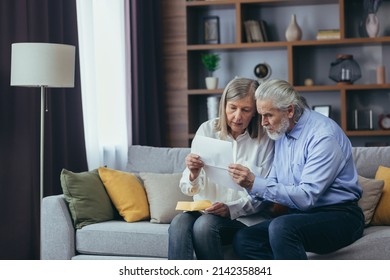 Angry Frustrated Document Senior Couple. Unhappy Old Family Getting Stressed. Serious Older Husband Showing Banking Paper Document Bills Taxes To Confused Elderly Wife In Home. Worried Looking Utility