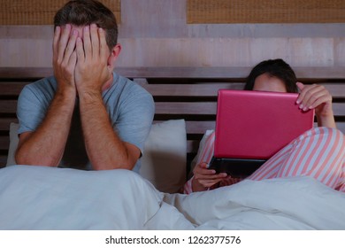 Angry And Frustrated Husband Moody In Bed Ignored By His Workaholic Wife Or Internet Social Media Addict Girlfriend Using Laptop In Bed Ignoring The Man In Couple Problem And Internet Conflict