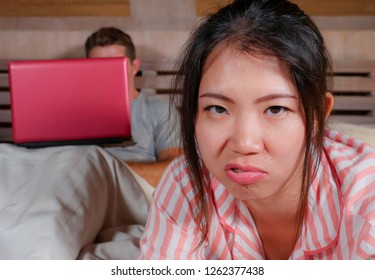 Angry And Frustrated Korean Woman In Bed Ignored By Workaholic Husband Or Internet Social Media Addict Boyfriend Networking With Laptop In Bed Ignoring The Woman In Asian Couple Problem Conflict