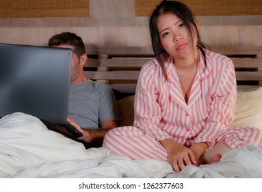 Angry And Frustrated Korean Woman In Bed Ignored By Workaholic Husband Or Internet Social Media Addict Boyfriend Networking With Laptop In Bed Ignoring The Woman In Asian Couple Problem Conflict