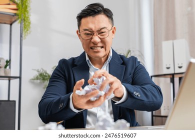 Angry furious Asian businessman working at office throwing crumpled paper nervous breakdown at work, brainstorming, stress management, mental distress problems, losing temper, reaction on failure - Powered by Shutterstock