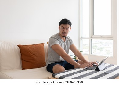 Angry And Furious Asian Trader Man Working On Tablet Or Laptop In His Apartment.