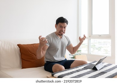 Angry And Furious Asian Trader Man Working On Tablet Or Laptop In His Apartment.