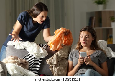 Angry Girl Scolding Her Messy Roommate Sitting On A Couch In The Living Room At Home