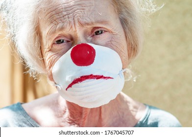 Angry Grandmother Elderly Woman In A Respiratory Mask With A Painted Funny Clown Mask. Tired Of Wearing A Mask. Old Lady Makes Fun Of Wearing A Mask, Covid-19. Concept Of Deception Coronavirus