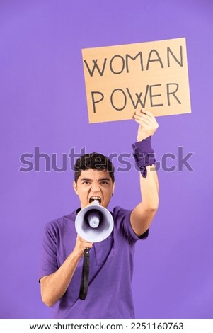 Angry hispanic protestor shouting on megaphone for equality and holding billboard with woman power message isolated on purple background