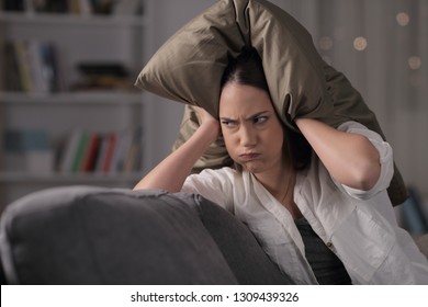 Angry homeowner suffering neighbor noise covering ears sitting on a couch in the night at home