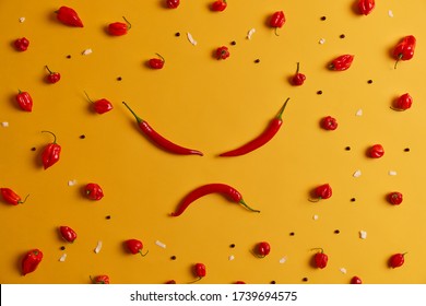 Angry Human Face Made Of Red Chili Pepper, Other Peppers Arranged Around On Yellow Background. Spicy Vegetable That Can Trigger Burning Sensation And Cause Health Problems, Has Own Distinct Taste