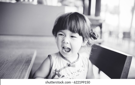 Angry And Hungry Little Asian Girl Is Screaming In Restaurant.angry Kid.Facial Expression.black And White Tone.