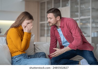 Angry husband threatening sad wife. Girl covering face with hands, wiping away tears, while guy in offensive pose viciously explaining, discussing. Woman victim and cruel man fighting squabbling. - Powered by Shutterstock