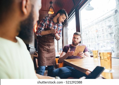 Angry irritated bearded man arguing with waiter about his bill in bar