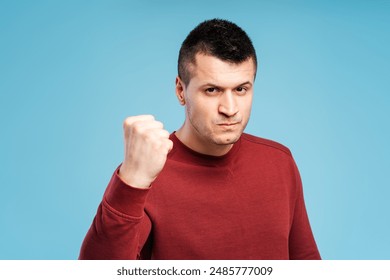 Angry, irritated young man in red sweatshirt showing clenched fist, showing anger standing isolated on blue background. Conflict concept - Powered by Shutterstock