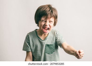 Angry Kid Shouting And Rising His Fist. Aggressive Little Boy With Mouth Wide Open Looking To The Camera. ADHD Syndrome