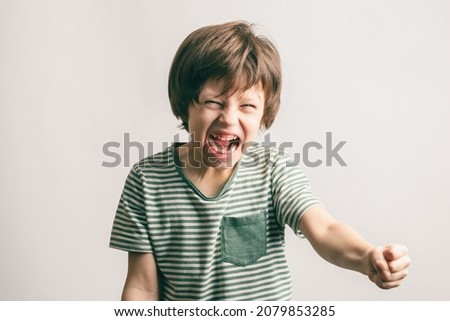 Angry kid shouting and rising his fist. Aggressive little boy with mouth wide open looking to the camera. ADHD syndrome