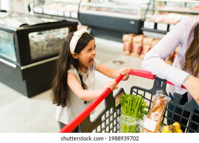 Angry little kid screaming and throwing a tantrum while grocery shopping with her mom at the supermarket because she won't buy her candy