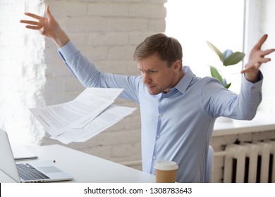 Angry mad businessman sitting at workplace throwing documents paper feels nervous unable control emotions and handle the stress at work. Bad day, problems in business huge debts and bankruptcy concept