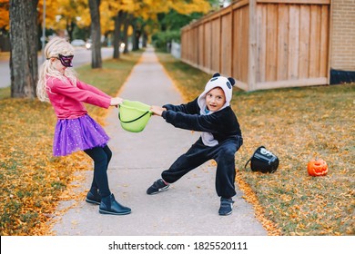 Angry Mad Children Fighting For Basket. Funny Trick Or Treat On Halloween Holiday. Kids Boy And Girl Friends In Party Costumes Can Not Share Holiday Candies And Treats. Siblings Family Relationship.