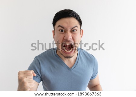 Angry and mad face of Asian man in blue t-shirt on isolated background.